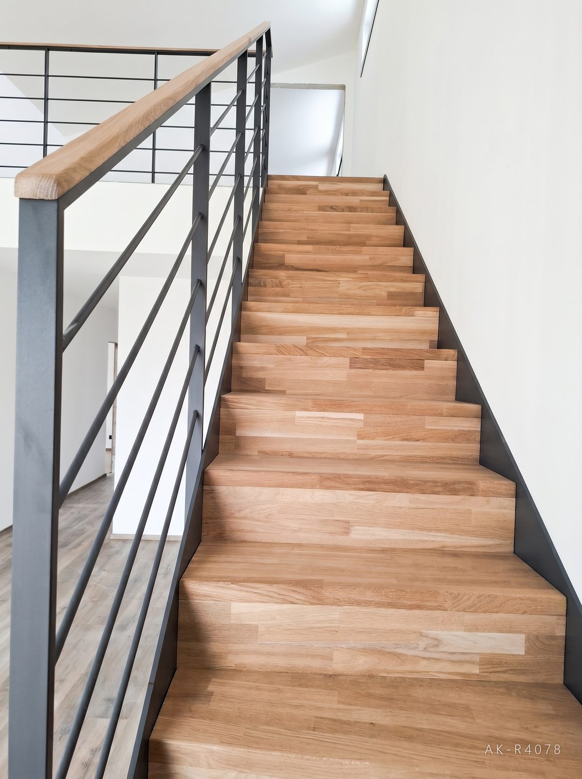 Lomené schodiště s podstupnicemi, antracitové schodnice a zábradlí. Vytváří prostor pro plánovanou kuchyňskou linku v minimalistickém rodinném domě v Ejpovicích, foto 5/5