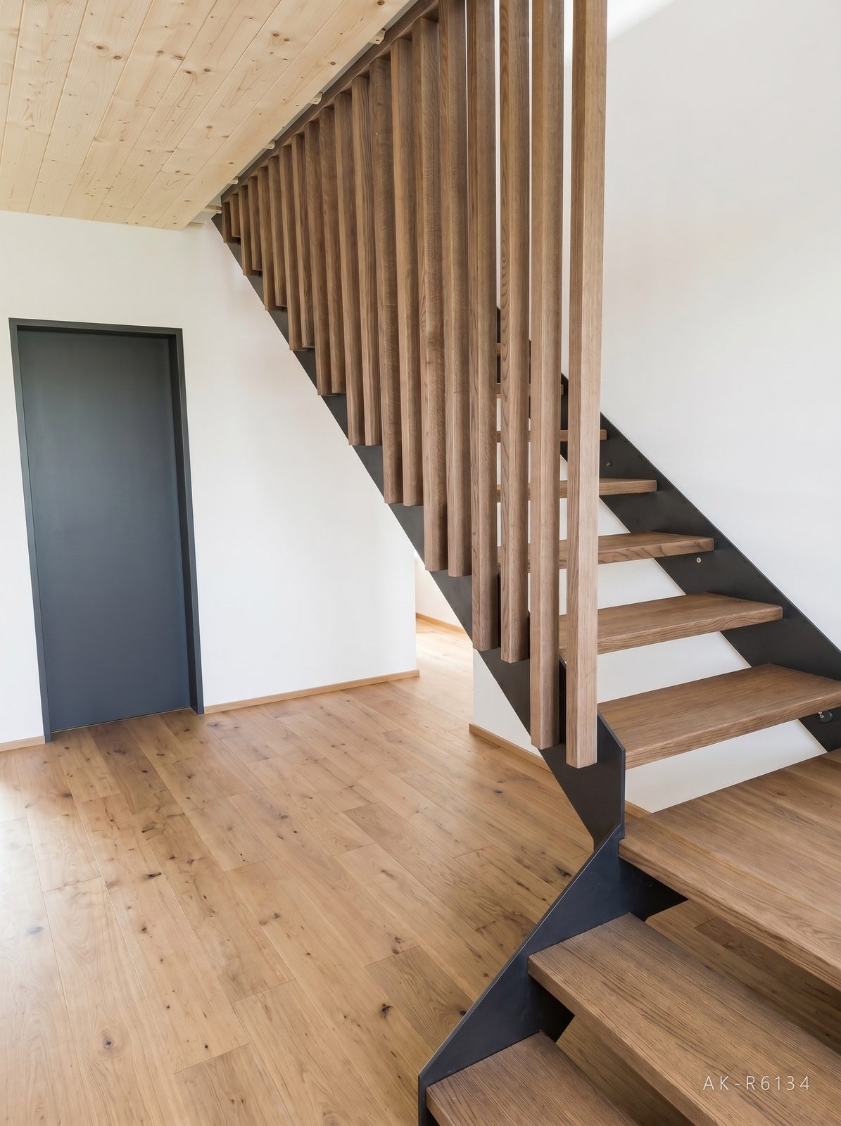 Přímé schodnicové schodiště s nástupní podestou, boční schodnice z černé oceli, dřevěné stupně s podsvícením, zábradlí ze svislých dřevěných lamel kotvených do stropu, foto 3/5